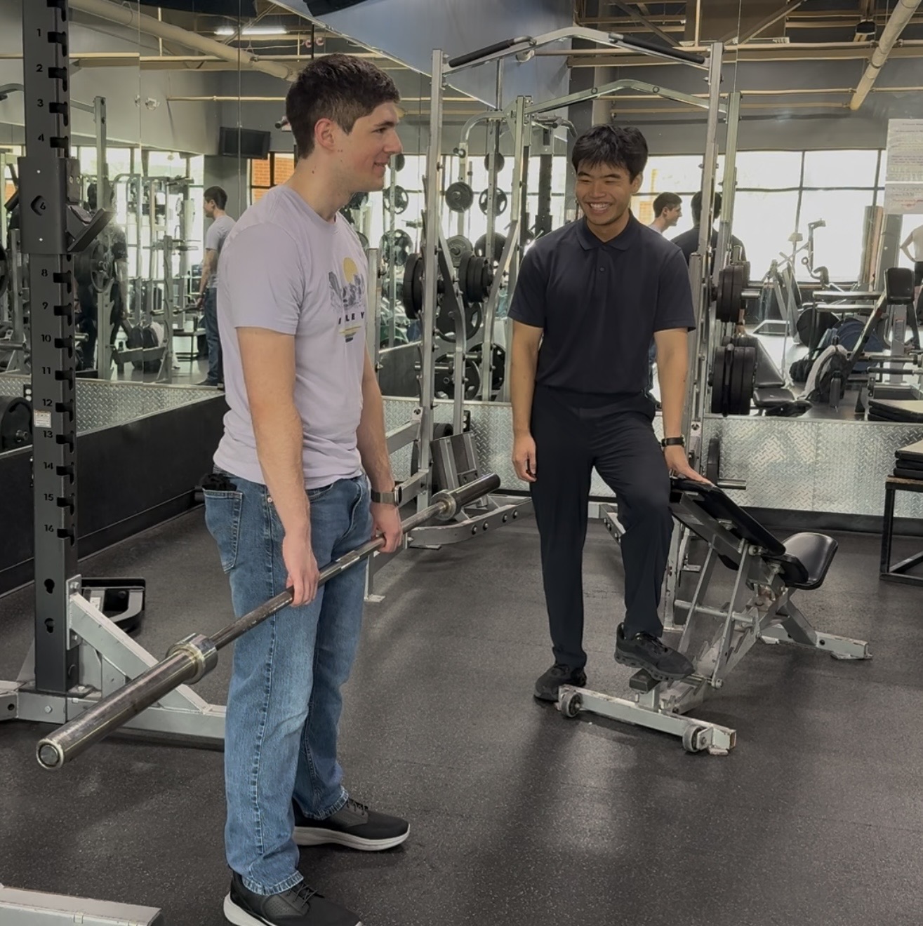 Gavin Bender and Jimmy Xiao on the gym floor, mid-conversation over a loaded bar.